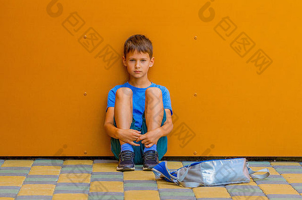 伤心男孩坐着色彩斑斓的墙在户外