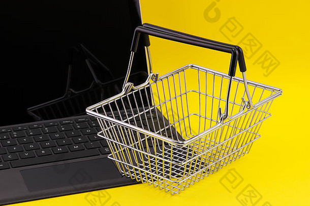 网络购物的概念是一台笔记本电脑，其键盘上有一个迷你购物车篮，与黄色背景隔离