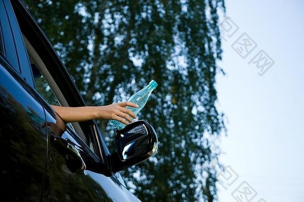 年轻的女人扔空塑料瓶开放车窗口视图背景模糊的树天空复制间距