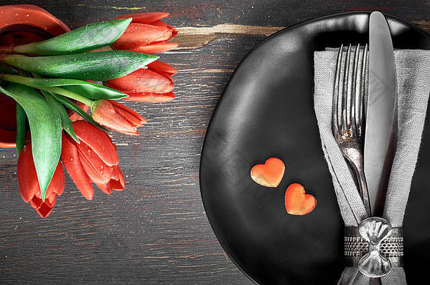 春季菜单概念。黑色盘子、黑色餐巾、带有红色郁金香和装饰心形的复古餐具。