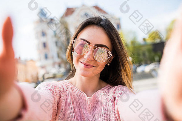 在阳光明媚的街道上，一名年轻女子手持手机拍摄自拍。