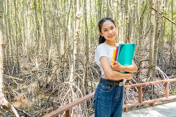 在红树林里，一个女孩胸前放着三本书。