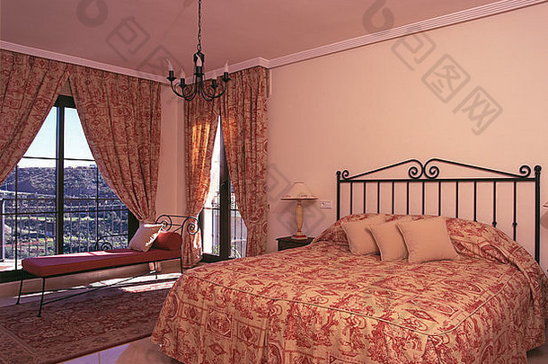 西班牙卧室的金属床上有粉案的被子，阳台的玻璃门上有协调的窗帘
