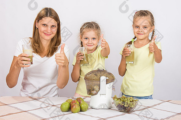 年轻漂亮的母亲和两个女儿坐在桌旁，用榨汁机从梨和葡萄中榨汁