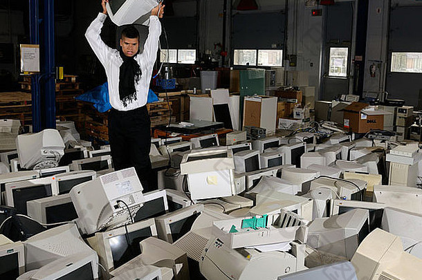 愤怒的男子在堆满过时电脑的仓库中举起旧电脑显示器