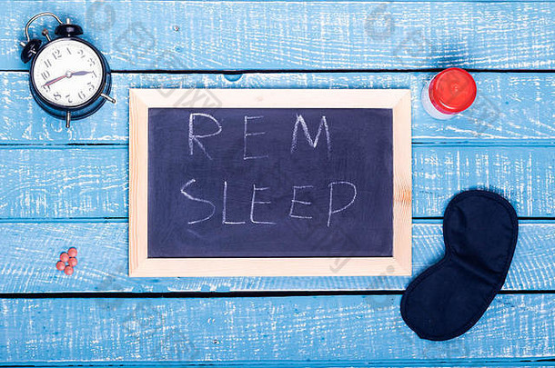 睡眠概念显示报警时钟睡觉药片眼睛面具黑色的董事会阅读快速眼动睡眠饱经风霜的蓝色的背景