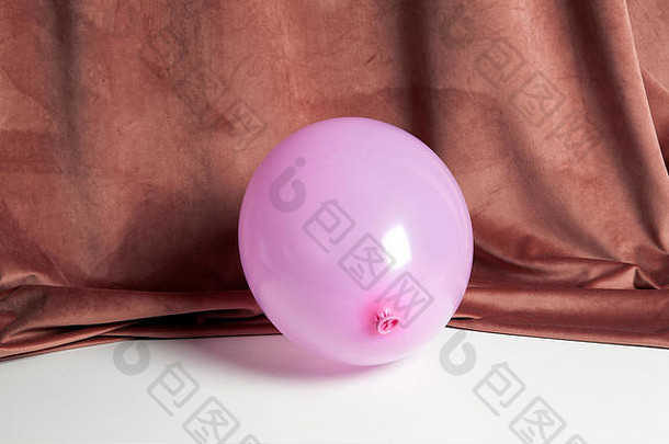 一个粉红色的充气气球在前面和粉红色的天鹅绒窗帘下面。色彩和谐。最小静物彩色摄影