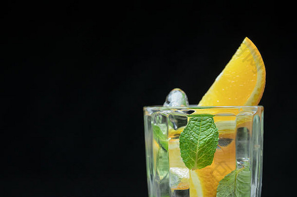 健康的排毒水与橘子和薄荷。黑色背景的夏日清爽饮料特写镜头。柑橘鸡尾酒。