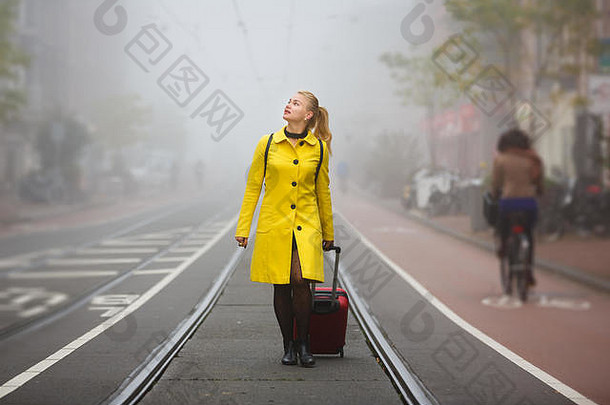 雾蒙蒙的秋天，带着手提箱的旅行者走在阿姆斯特丹市的街道上