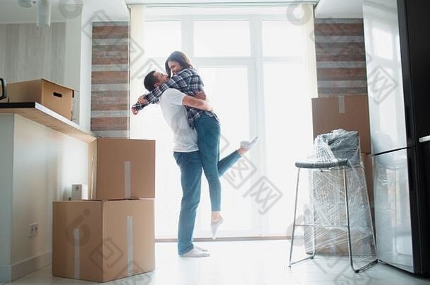 这对年轻夫妇第一次庆祝搬家日的概念，男人丈夫举着妻子站在<strong>新居</strong>公寓的箱子附近