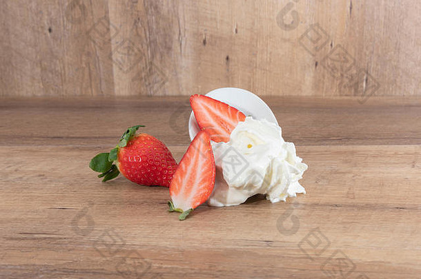 融化的鲜奶油和草莓放在白色盘子上，木制背景-图片