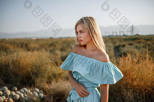 日落时，一位身穿浅蓝色连衣裙的年轻美丽的白人金发女孩站在<strong>西瓜地</strong>上，草<strong>地</strong>被晒干