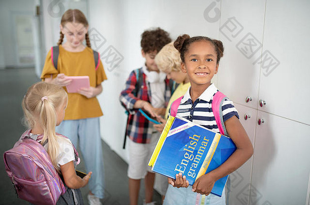 黑皮肤的女孩拿着英语语法书站在朋友旁边