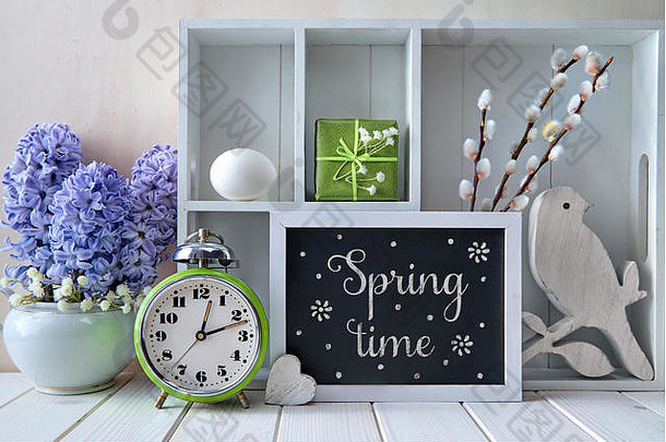 白色背景，春季装饰。旧闹钟，蓝色风信子花和不同物品的陈列柜。粉笔文字春天