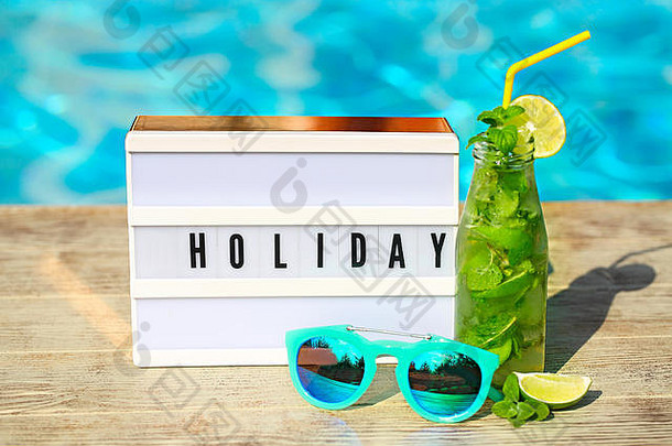 浅色信箱，印有“假日”字样、帽子、太阳镜和泳池背景上的酸橙莫吉托鸡尾酒