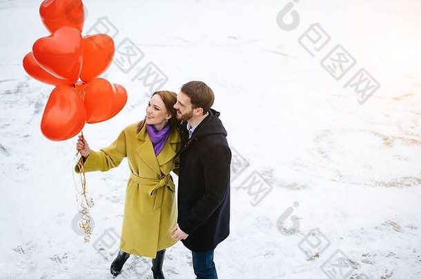 一对快乐的高加索夫妇在户外度过闲暇时光，他们穿着外套，手里拿着红色的气球。爱情、关系概念