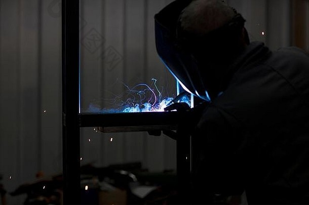 一位专注的焊工设计师戴着头盔，晚上在他的车间里一边焊接金属片，一边美丽的烟雾，完成了一个项目