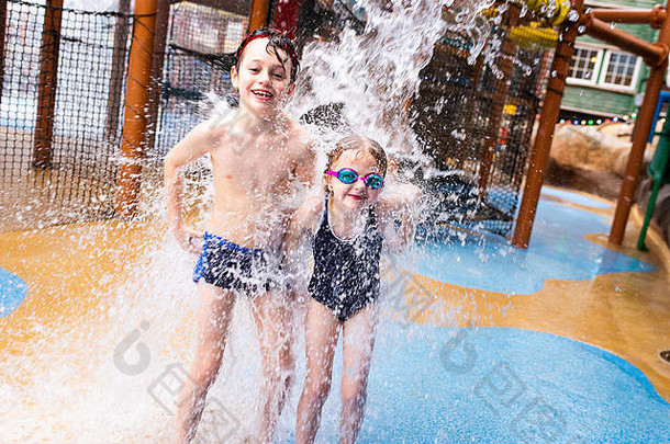 一个患有多动症、自闭症、阿斯伯格综合症的小男孩和他的妹妹在高压喷水器下玩耍，在飞溅物降落时笑得很开心，