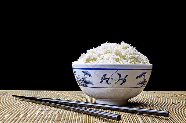 一碗煮熟的天然有机茉莉米饭，放在东方碗里，用筷子在黑色背景上摆放