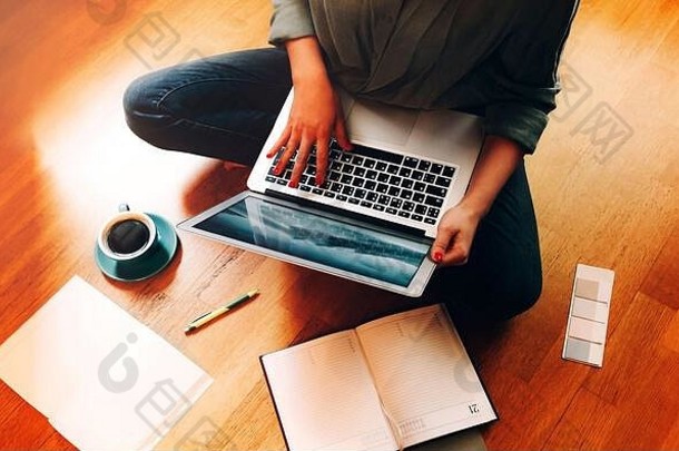 匿名女自由职业者坐着地板上杯咖啡开放规划师浏览移动PC工作设计项目他