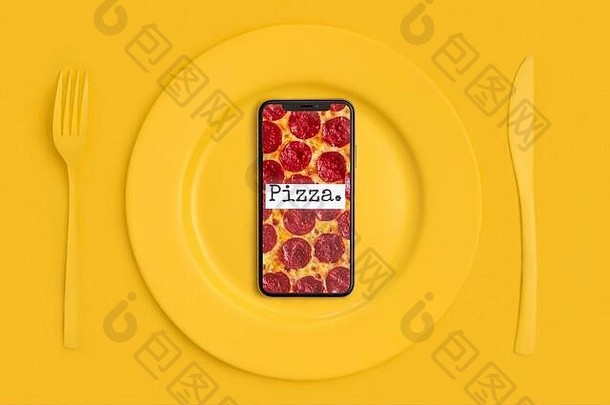 网上订餐，送货。打电话把食物带回家。屏幕上有比萨饼的智能手机，放在盘子上，刀叉上。黄的景色