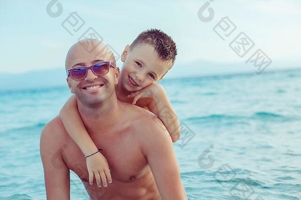 儿子和父亲微笑着，拥抱着对方，户外，海洋背景，一个快乐的家庭在度假。