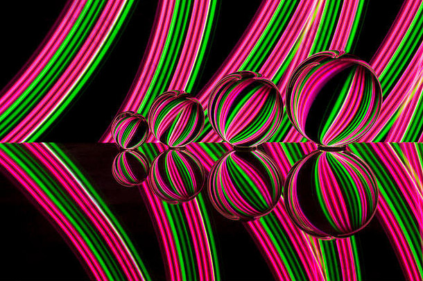 四个不同大小的水晶球/玻璃球/透镜球排成一行，在黑色背景上反射，后面有粉色和绿色的霓虹灯条纹