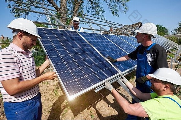 在阳光明媚的夏日，一个由四名技术人员组成的团队正在农村外部光伏太阳能电池板系统。可再生生态廉价绿色能源生产理念。