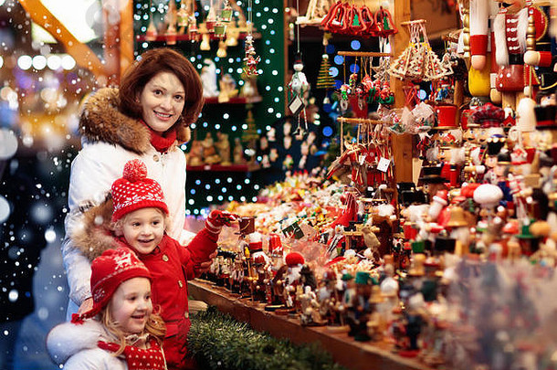 戴着暖帽的母亲和孩子在传统的德国圣诞街市场观看手工制作的玻璃圣诞树装饰品。一家人带着孩子去购物