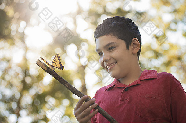 一个男孩拿着一根棍子，棍子上栖息着一只五颜六色的蝴蝶。