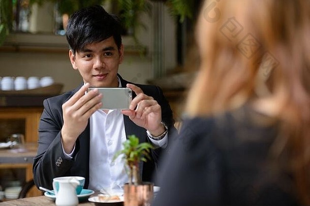 一对年轻的亚洲商人夫妇在咖啡馆与一名男子用手机拍照