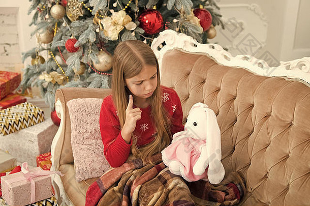 你应该听我说。小女孩在圣诞树上教可爱的兔子。小孩把手指指向柔软的玩具。小女孩抱着兔子玩具。带礼物的小孩。最好的圣诞玩具。
