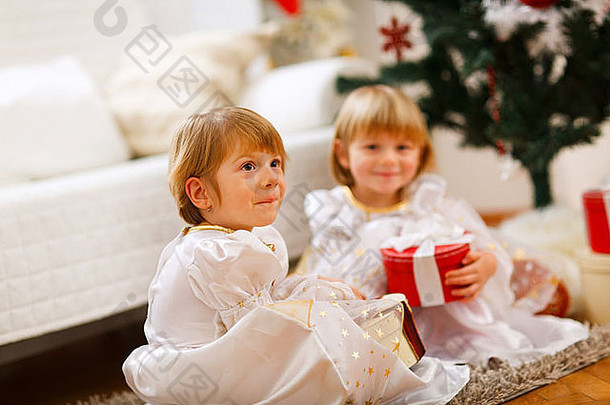双胞胎女孩坐着礼物圣诞节树