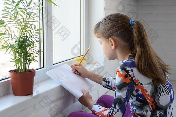 一个少年坐在窗前的地板上，用铅笔在<strong>画册</strong>上画画