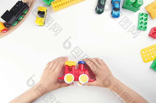 俯视图：白色桌子背景上，孩子的手在玩玩具火车和许多玩具。