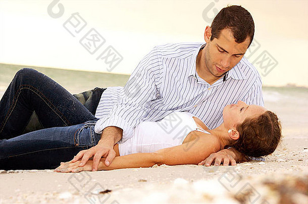 美丽的年轻夫妇躺在沙滩上聊天，他们的衣服被海水打湿了