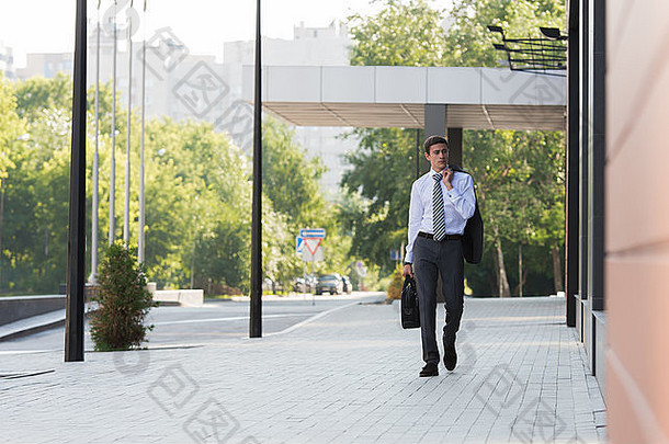 一位英俊的商人在办公楼附近的街道上行走的肖像