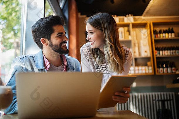 这对年轻夫妇正在咖啡馆里用笔记本电脑工作，面带微笑。