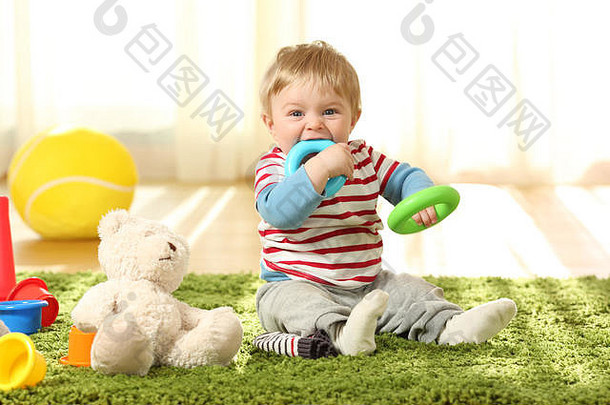 一个快乐的婴儿在家里的地毯上咬玩具的正面照片