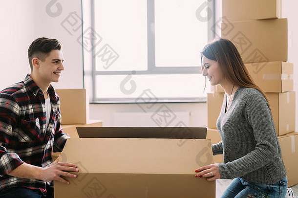 一对微笑的年轻夫妇在一所新房子里打开纸箱，他正在桌子上的一个大盒子里搜寻物品
