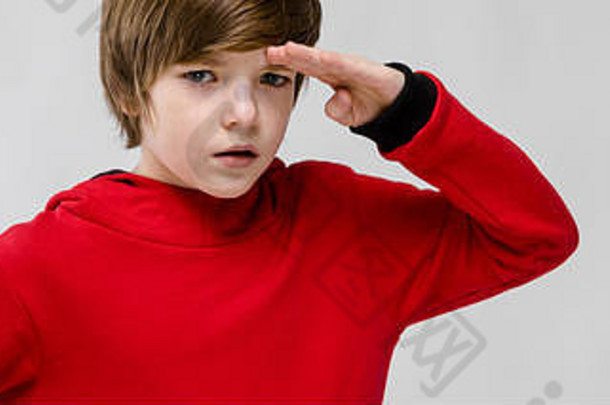 穿着红色毛衣的可爱自信的白人小男孩在灰色背景下遥望远方