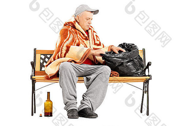 无家可归的成年人坐在长椅上，在包里找东西