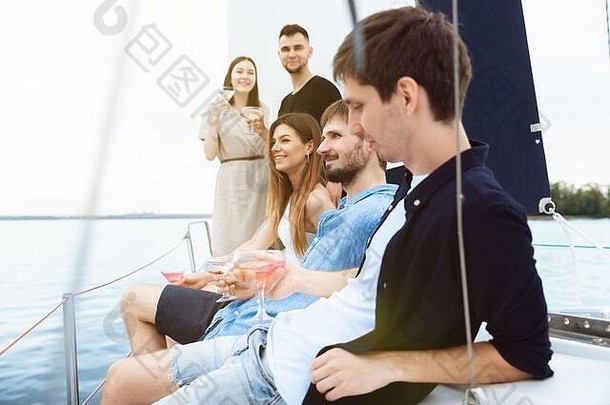 一群快乐的朋友在户外的船上聚会上喝着伏特加鸡尾酒，兴高采烈。年轻人享受海游、青春和暑假的乐趣。喝酒、度假、休息。