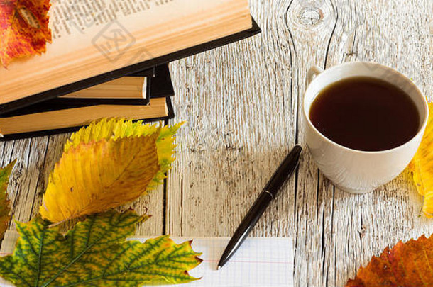 在白色木质背景上，用钢笔、杯子和秋叶打开书本和笔记本