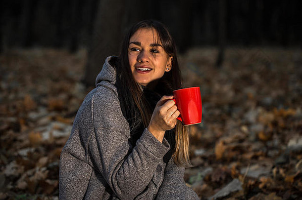 美丽的女孩在秋天的森林里喝着一杯热茶，秋意盎然