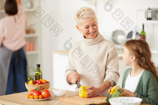 快乐美丽的祖母切割蔬菜微笑（外）孙女帮助烹饪<strong>厨房</strong>