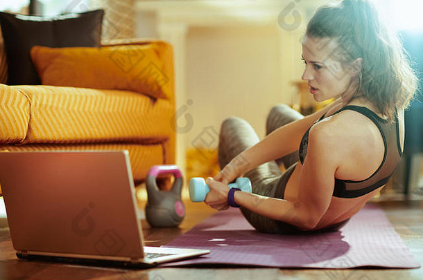 健康的女人健身衣服在线流媒体健身网站移动PC练习哑铃健身席现代房子