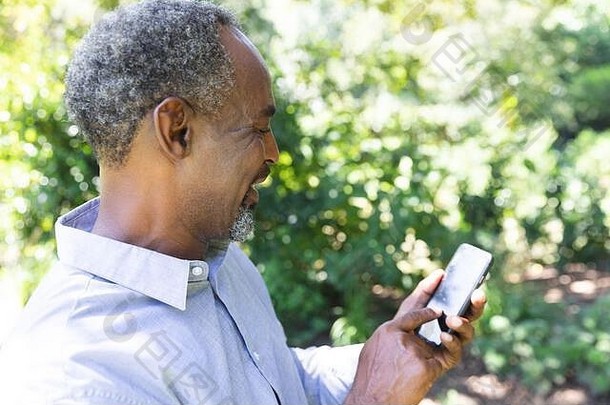 一位非洲裔美国老人在花园里使用手机的侧视图