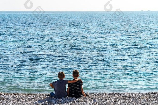 两个男孩坐在海滩上，往海里<strong>扔石头</strong>