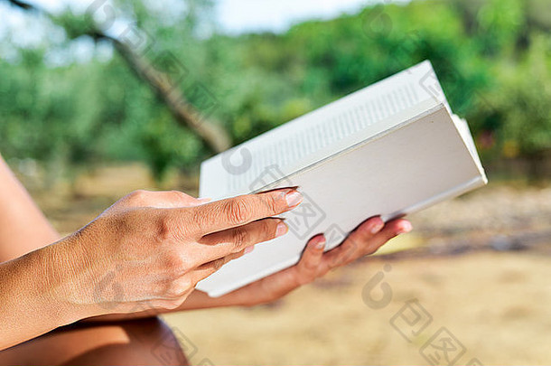 特写镜头：一位年轻的白人妇女在阳光明媚的日子里，在户外自然景观中看书